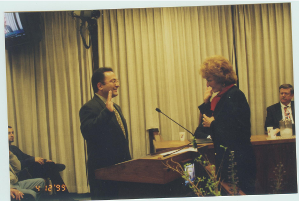 Top half of image is a man standing in a room with his right hand up. A woman is administering an oath. Bottom half is a news press clipping for an article titled "Actions that affect our lives". A man is standing in front of students speaking