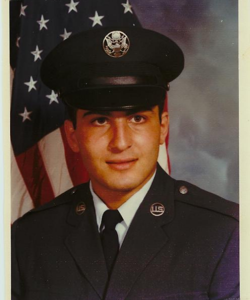 Rafi Manoukian in a United States Air Force uniform. Portrait with a grey background and an American Flag in the left corner